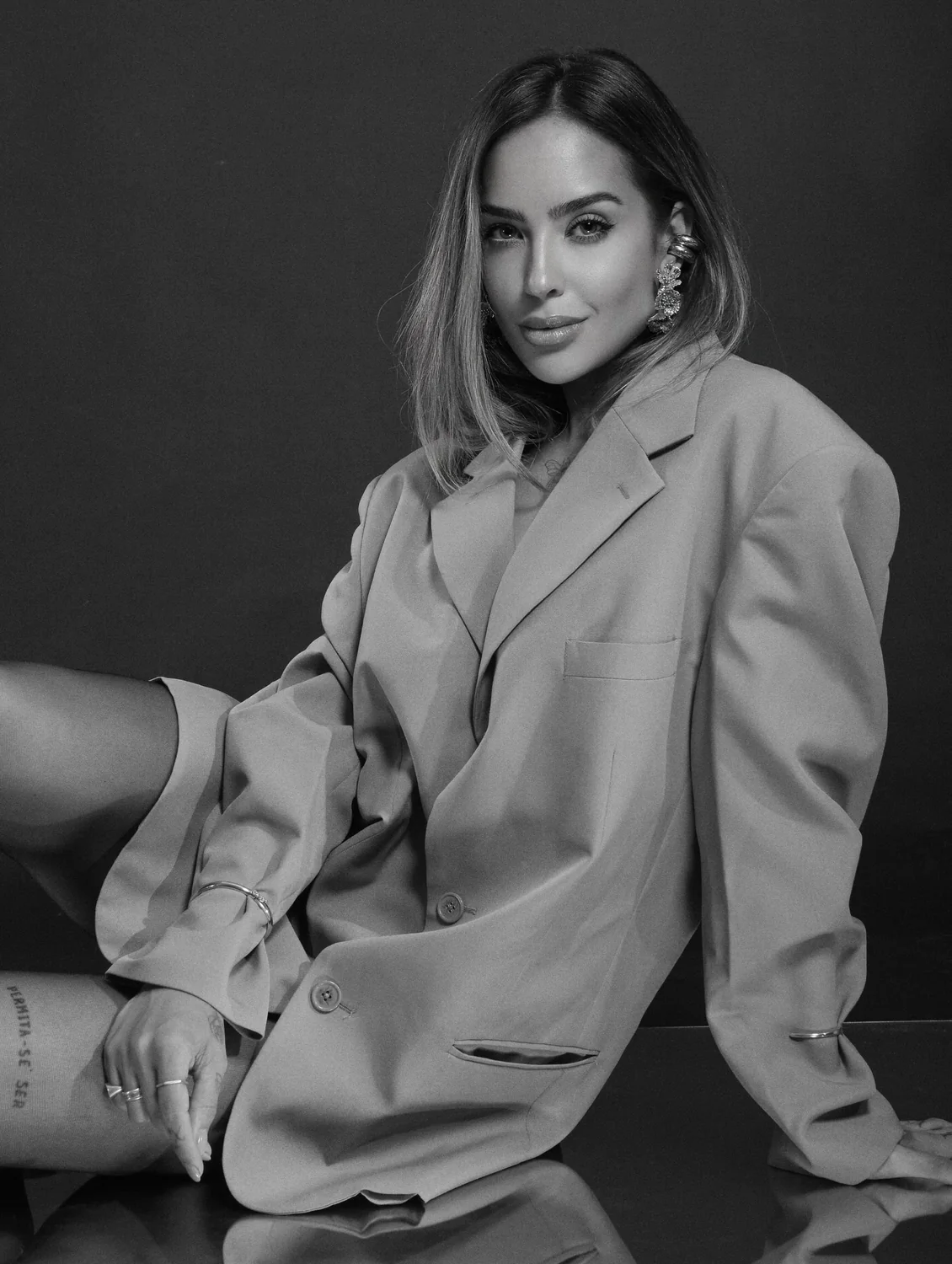 Retrato em preto e branco de Julia Melo com blazer oversized, sentada no chão de um estúdio.